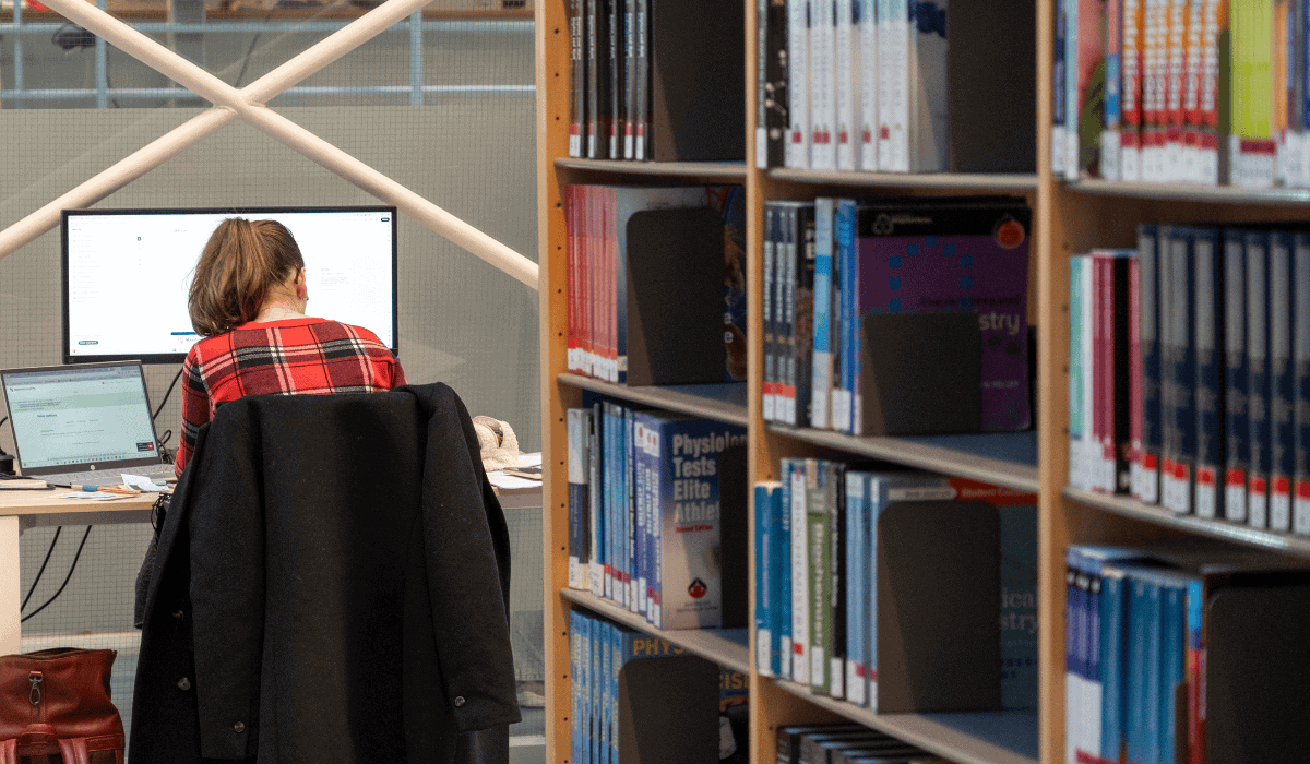 1. Student studying at Maastricht University Library with bookshelves in background.