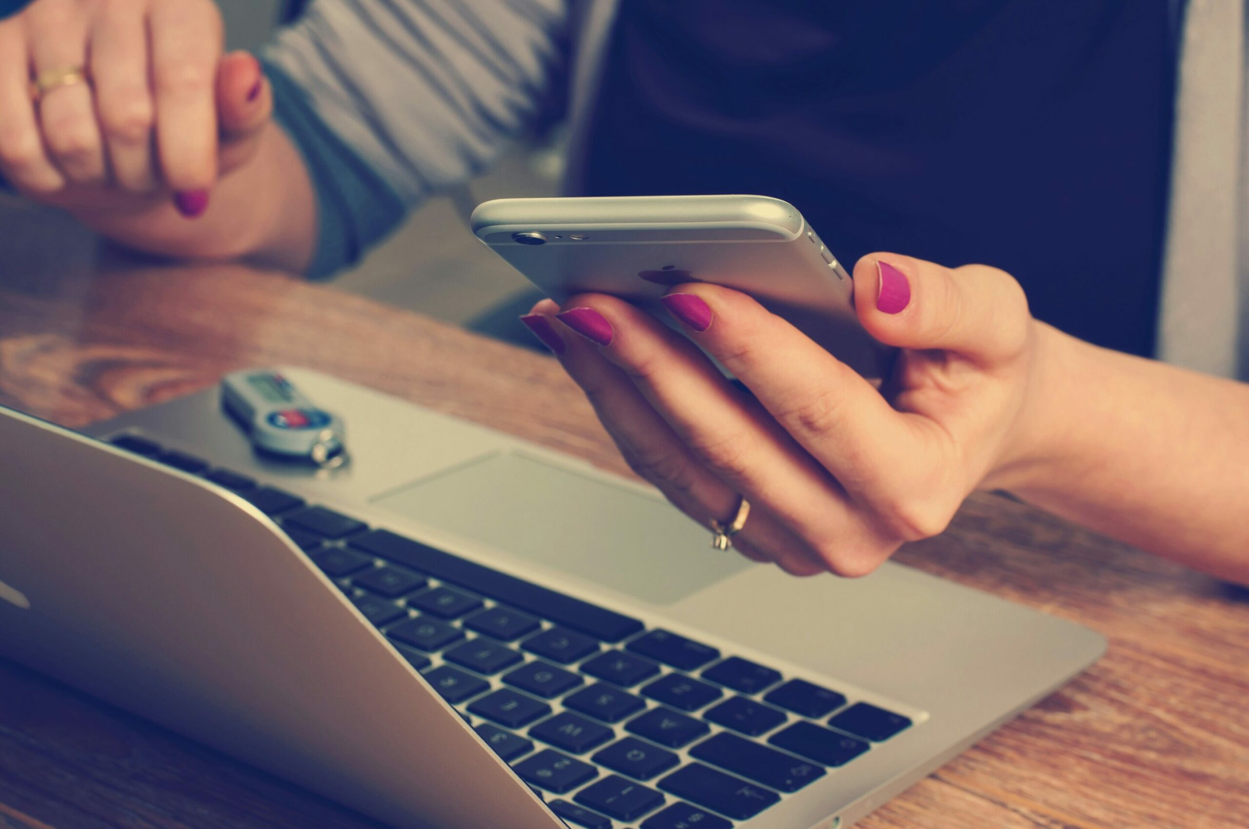 a hand holding an iphone and a laptop