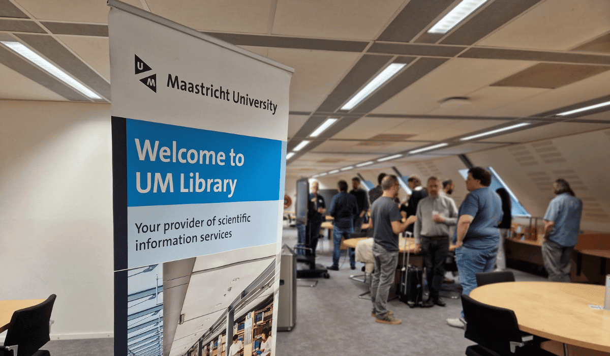 People gather at a library event with a Maastricht University banner in the foreground.