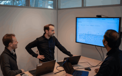 Three men in a meeting room discussing data on a large screen.