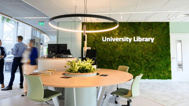 Modern library reception area with green wall and round table.
