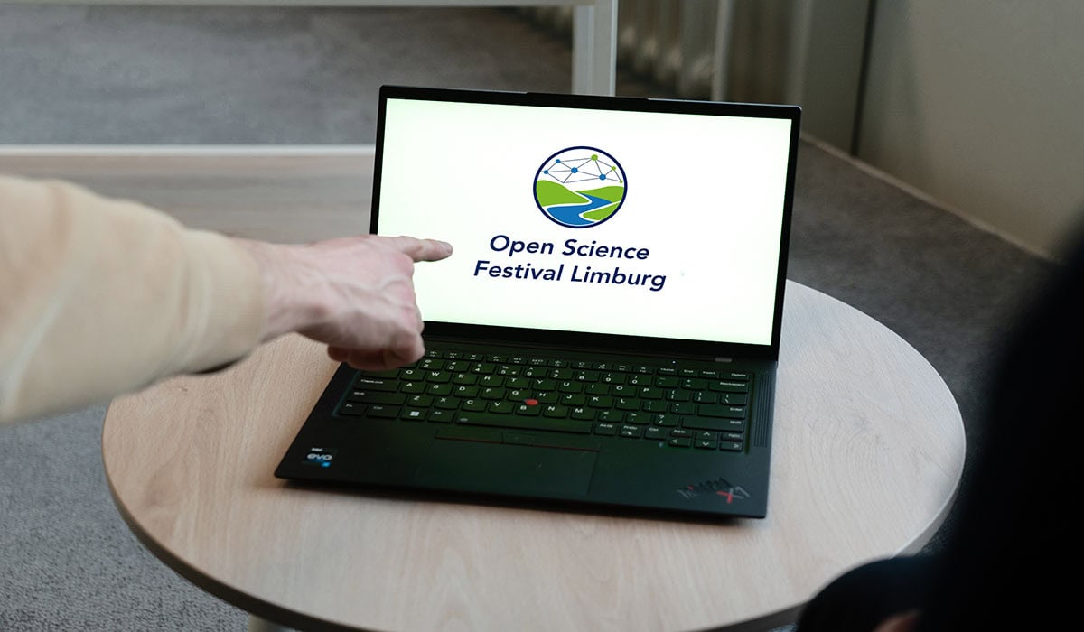 A person points at a laptop showing the Open Science Festival Limburg logo, promoting the upcoming event.