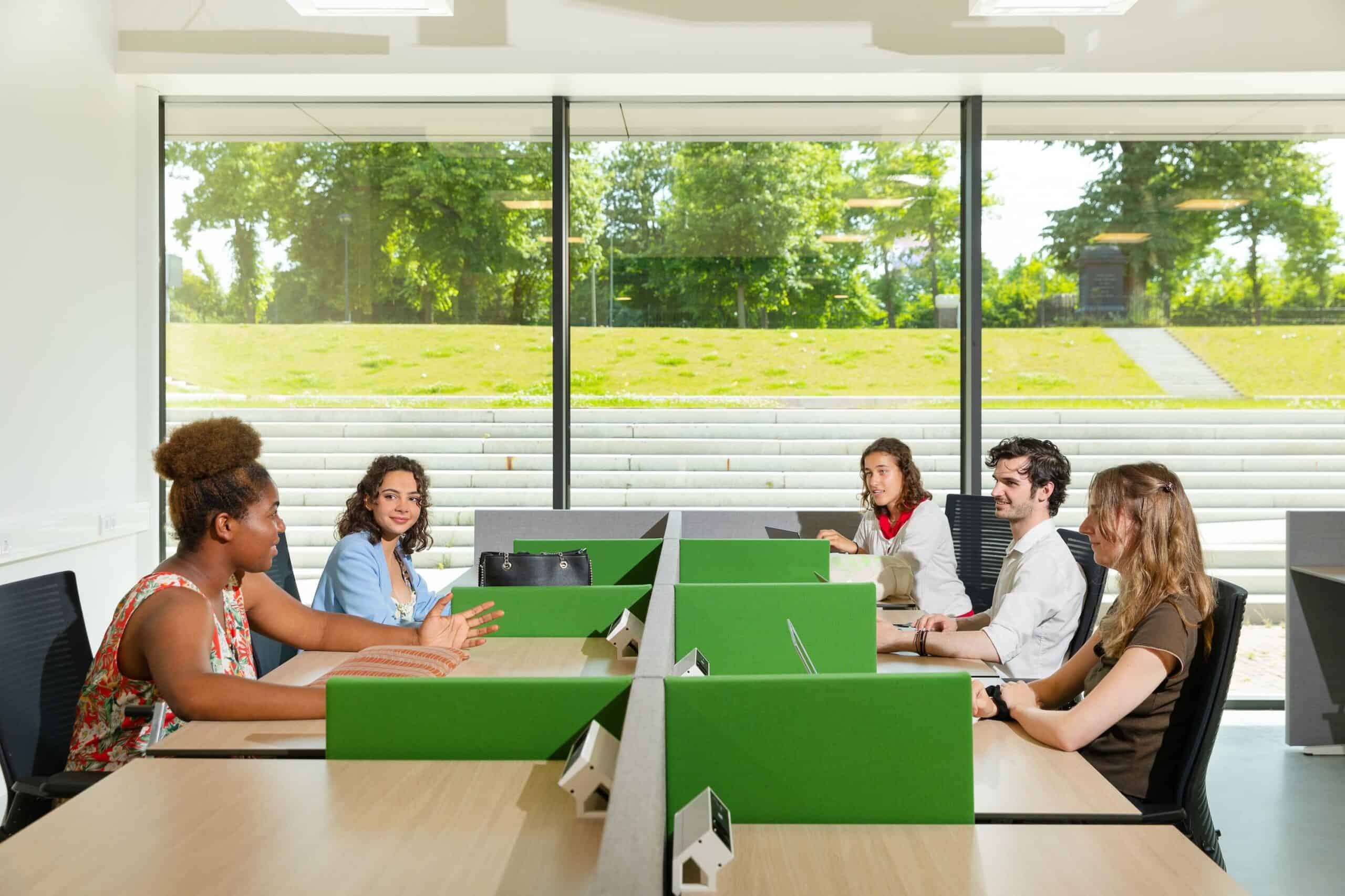 5 students are sitting on their own table while looking at each other and having a conversation