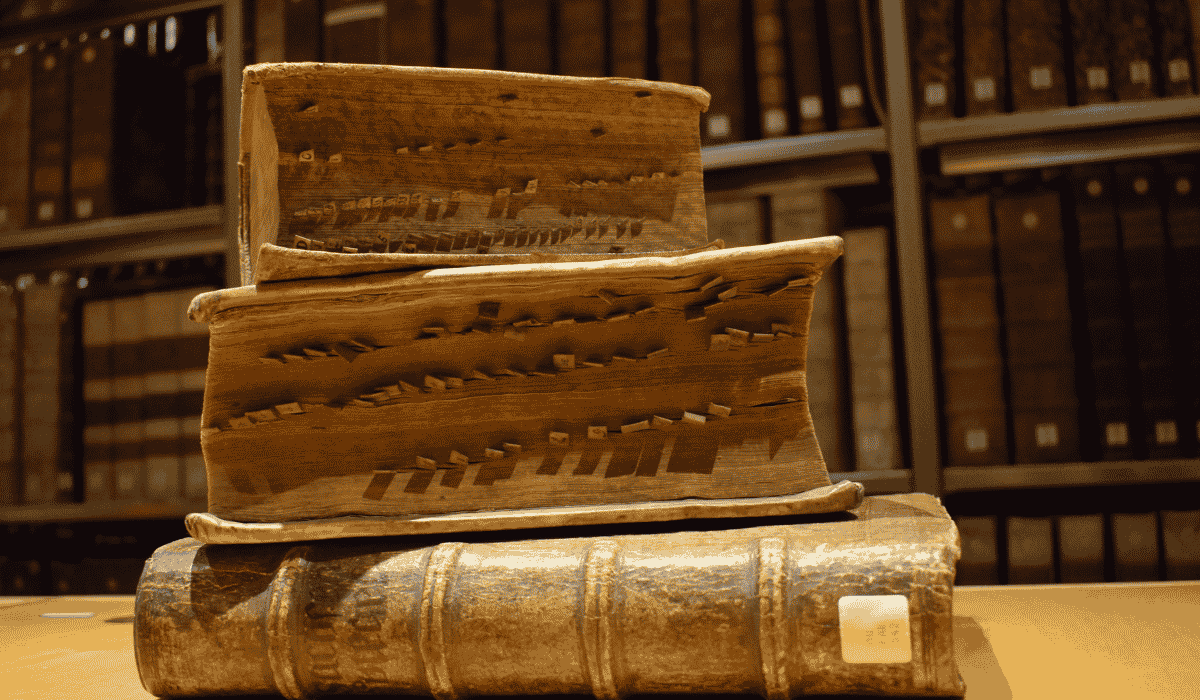 Ancient, damaged books on a wooden table in a library setting.