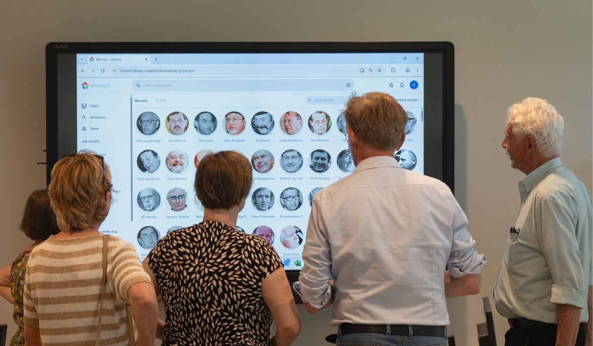 Several individuals gathered around a large digital screen displaying various profile images at Maastricht University Library.